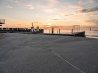 a man rides a skateboard down a pier near the ocean during sunset on a sunny day