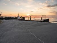 a man rides a skateboard down a pier near the ocean during sunset on a sunny day