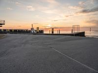 a man rides a skateboard down a pier near the ocean during sunset on a sunny day