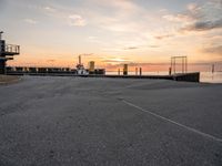 a man rides a skateboard down a pier near the ocean during sunset on a sunny day