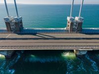 large metal pipes are coming from the water on an oceanfront bridge in a blue sky with blue clouds