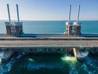 large metal pipes are coming from the water on an oceanfront bridge in a blue sky with blue clouds