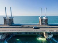 large metal pipes are coming from the water on an oceanfront bridge in a blue sky with blue clouds