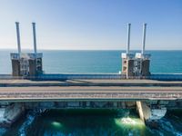 large metal pipes are coming from the water on an oceanfront bridge in a blue sky with blue clouds