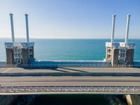 large metal pipes are coming from the water on an oceanfront bridge in a blue sky with blue clouds