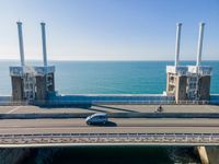 large metal pipes are coming from the water on an oceanfront bridge in a blue sky with blue clouds