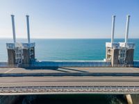 large metal pipes are coming from the water on an oceanfront bridge in a blue sky with blue clouds