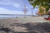 the sidewalk has stones on it near the water of the lake with trees and benches along it