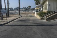 a long walkway leading to a beach with a boat docked near the water and a building behind it