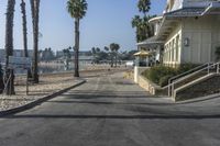 a long walkway leading to a beach with a boat docked near the water and a building behind it