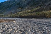 a man riding a bike down a gravel road next to a large mountain side next to a river