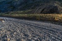 a man riding a bike down a gravel road next to a large mountain side next to a river