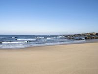 a beach with some waves and rocky shoreline next to it, with a blue sky above