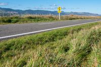 a road leading to the beach in front of mountains with tall grass and grass on it