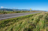 a road leading to the beach in front of mountains with tall grass and grass on it