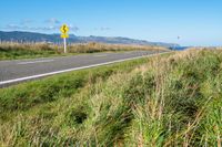 a road leading to the beach in front of mountains with tall grass and grass on it