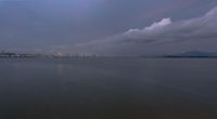 large body of water with buildings on the other side of it and storm coming in to the sky