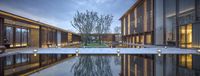 a courtyard with illuminated lighting surrounded by trees and lawn area with water features outside the buildings