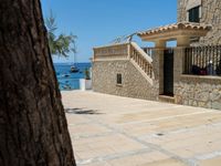 people looking at a home in front of the ocean with boats in the water and steps down to a stone building