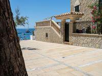 people looking at a home in front of the ocean with boats in the water and steps down to a stone building