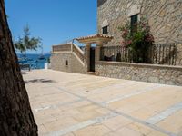 people looking at a home in front of the ocean with boats in the water and steps down to a stone building