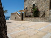 people looking at a home in front of the ocean with boats in the water and steps down to a stone building