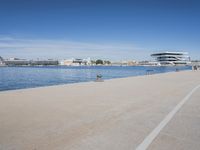 there is a very long walkway along the water near buildings and water features on a sunny day
