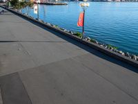 a long cement walkway lined with flags next to a body of water next to a sidewalk