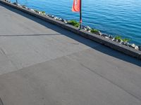 a long cement walkway lined with flags next to a body of water next to a sidewalk