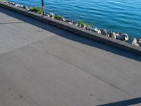 a long cement walkway lined with flags next to a body of water next to a sidewalk