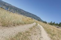 the trail winds through the dry grasses towards the water and mountains in the distance to the right