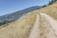 the trail winds through the dry grasses towards the water and mountains in the distance to the right