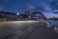 the view from across the road to the sydney harbour bridge in the dark blue hour