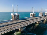 a bridge over the ocean with construction equipment in the background and two people walking on it