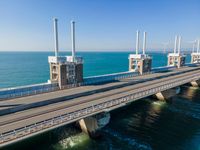 a bridge over the ocean with construction equipment in the background and two people walking on it