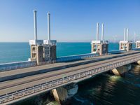 a bridge over the ocean with construction equipment in the background and two people walking on it