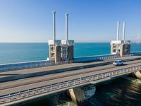 a bridge over the ocean with construction equipment in the background and two people walking on it