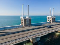 a bridge over the ocean with construction equipment in the background and two people walking on it