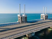 a bridge over the ocean with construction equipment in the background and two people walking on it