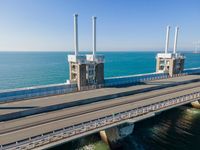 a bridge over the ocean with construction equipment in the background and two people walking on it