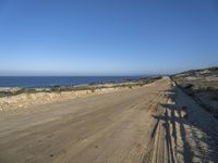 a dirt road lined with dry grass, and the ocean in the distance in the background