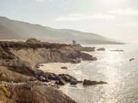 a lighthouse tower is perched at the edge of a mountain and the beach is in the distance