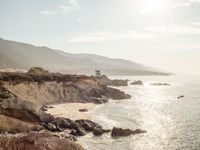 a lighthouse tower is perched at the edge of a mountain and the beach is in the distance