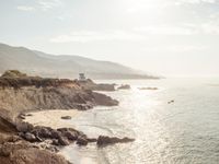 a lighthouse tower is perched at the edge of a mountain and the beach is in the distance