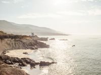 a lighthouse tower is perched at the edge of a mountain and the beach is in the distance