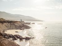 a lighthouse tower is perched at the edge of a mountain and the beach is in the distance