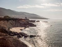 a lighthouse tower is perched at the edge of a mountain and the beach is in the distance