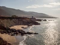 a lighthouse tower is perched at the edge of a mountain and the beach is in the distance