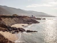 a lighthouse tower is perched at the edge of a mountain and the beach is in the distance