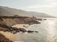 a lighthouse tower is perched at the edge of a mountain and the beach is in the distance